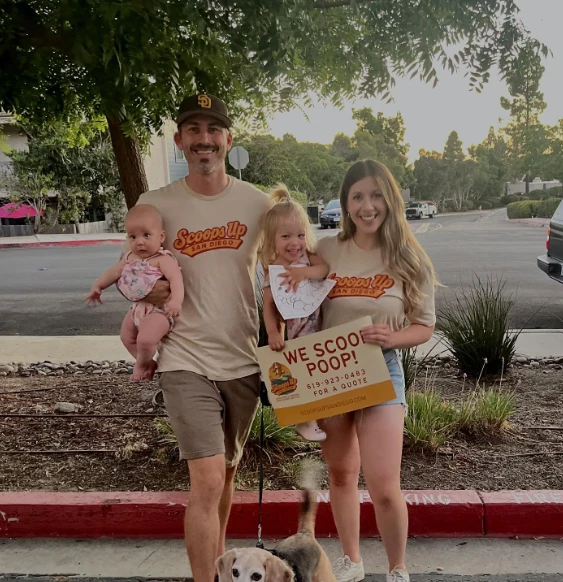 Corey Thomas and family in Scoops Up shirts, holding a “We scoop poop!” sign with their dog